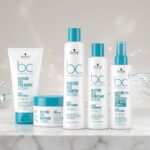 Commercial display of the Schwarzkopf Professional BC Bonacure Moisture Kick Clean Performance hair care line, featuring the Curl Bounce, Treatment, Shampoo, Conditioner, and Spray Conditioner on a marble surface with a hydrating water background.