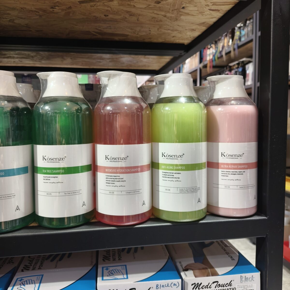 Four colorful Kósenze shampoo bottles on a black metal store shelf, displaying green, red, yellow, and pink colors.