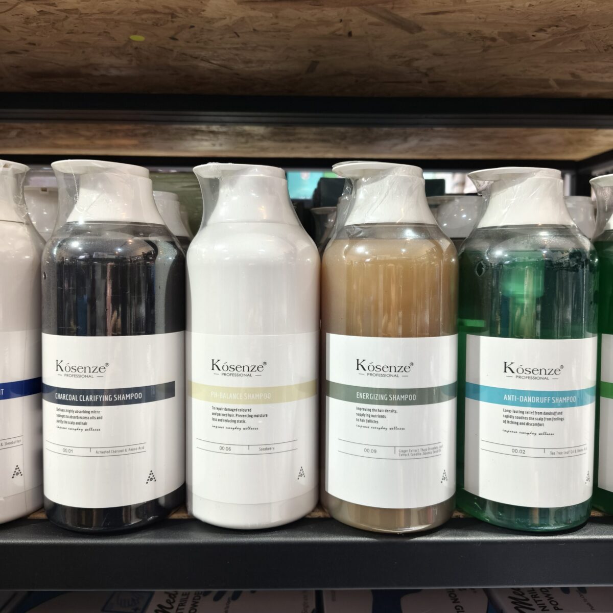 Retail display showing four Kósenze shampoo bottles in dark grey, white, amber, and teal green.