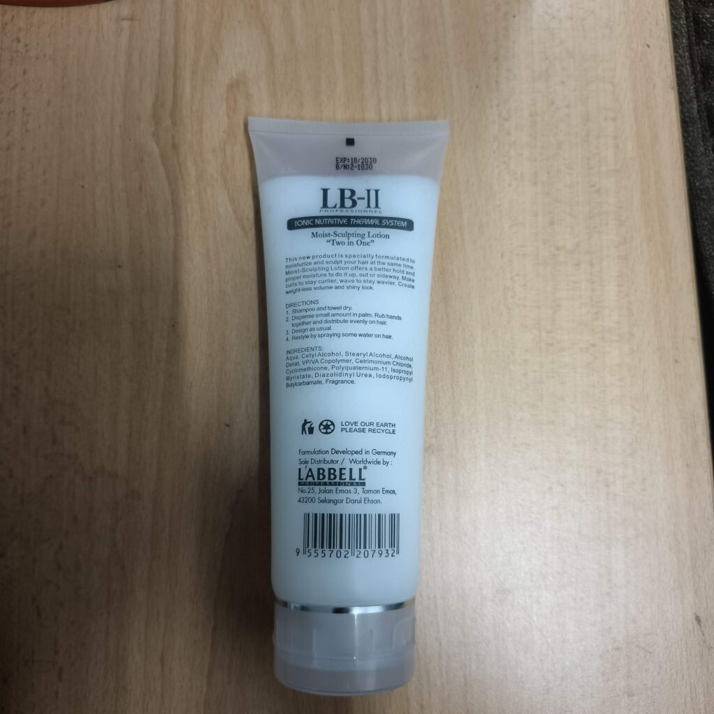 Back label of LB-II Professional Moist-Sculpting Lotion white squeeze tube on a light wood surface.