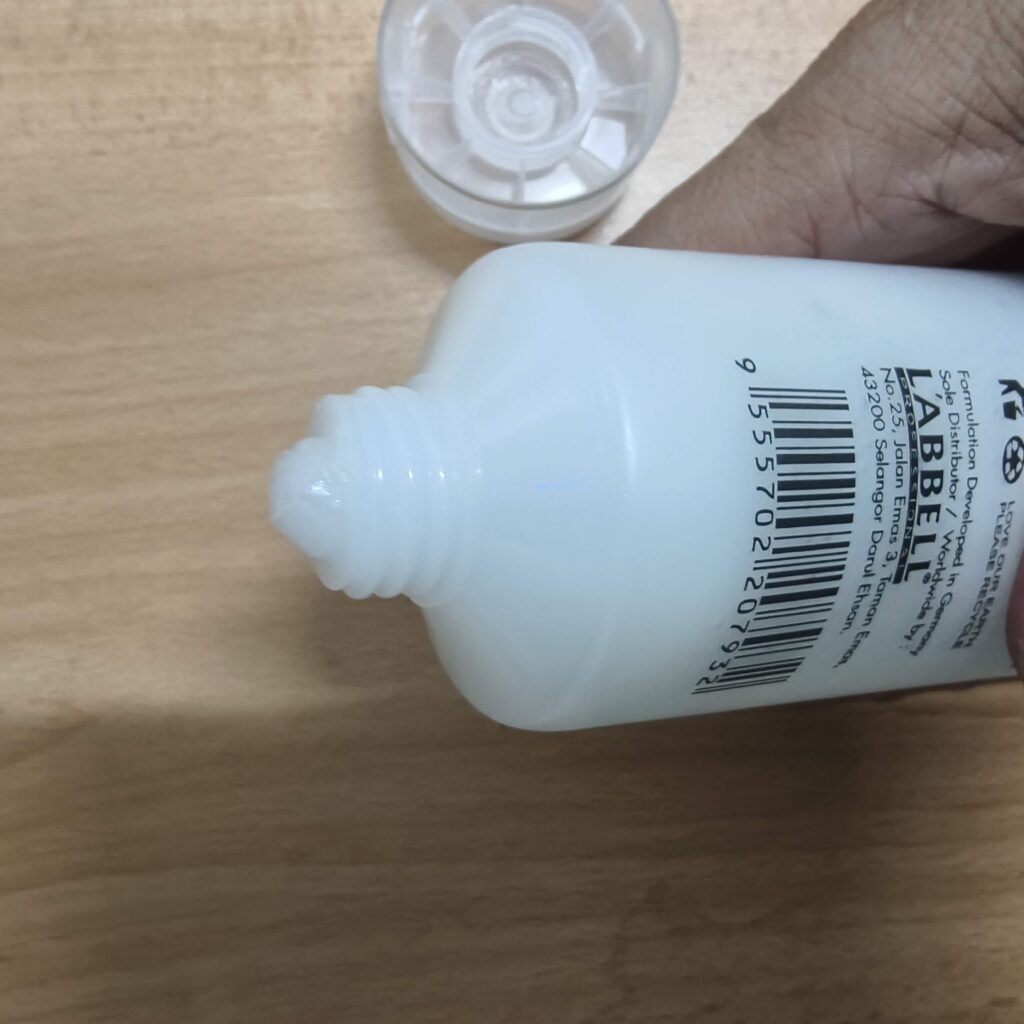 Close-up of the threaded nozzle and back label of a white L'ABBELL Professional squeeze tube held by a hand.