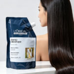 A sleek L'Oreal X-Tenso Oleoshape hair straightening cream bottle on a clean white marble surface, next to a woman with long super straight silky shiny Asian hair flowing down, soft studio lighting, high-end product photography, before-after concept, minimalist and elegant