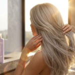 Editorial-hair-campaign-photography-side-back-portrait-of-a-woman-with-ash-blonde-bleached-long-hair-bathed-in-bright-natural-golden-hour-sunlight-by-a-window
